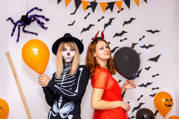 Two young women dressed as a devil and a skeleton have fun and pose for the camera on Halloween.