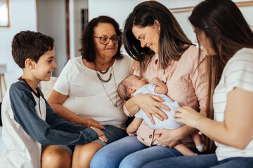 Multi-generation family sitting on sofa with newborn baby