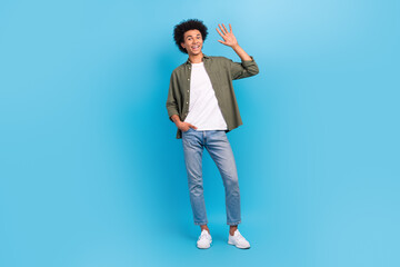 Fototapeta na wymiar Full body size photo of young friendly man wear khaki shirt jeans nike sneakers waves hand greetings isolated on blue color background