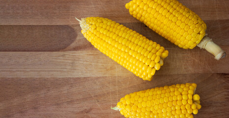 Rustic close-up of fresh yellow corn cobs arranged on natural wood — a versatile food-themed still life ideal for agricultural, culinary, or healthy eating content with editorial potential.