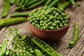 Green peas in closed and open pods, peeled peas in a bowl, scattered pea seeds on a wooden background.
