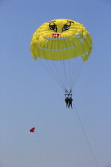 Budva, Montenegro - June 22, 2023: Parasailing in a blue sky near Budva beach, yellow parachute with people