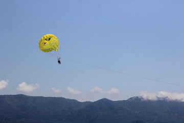 Budva, Montenegro - June 22, 2023: Parasailing in a blue sky near Budva beach, yellow parachute...