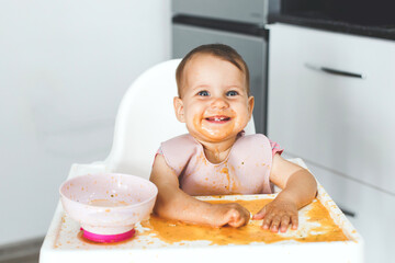 happy cheerful messy baby sits in a highchair and eats lure vegetable puree soup, the concept of baby food and childhood