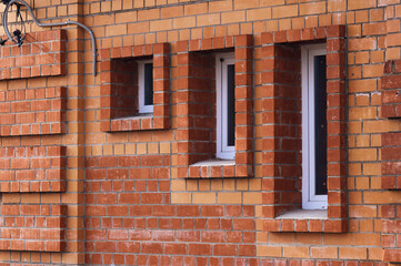 Minimalistic shot of a brick wall with windows of various sizes. Three windows with plastic frame. Red brick masonry. Facade of a building of unusual design.