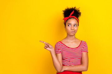 Photo of doubtful unsure girl dressed red striped t-shirt looking pointing finger empty space isolated yellow color background