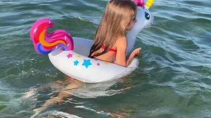 Happy baby girl swimming on an inflatable swimming unicorn in the sea