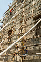 Filipino workmen on bamboo scaffolding,redecorating the end wall of Oslob Church,high above the ground,Cebu,Philippines.