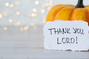 Thank You LORD, handwritten message on note and autumn pumpkin fruit on wooden table with white...