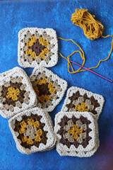 Crocheted granny squares made of natural brown, mustard and beige wool. Soft and fluffy crochet ornament on blue textured background. 