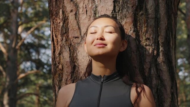 Young Asian woman meditating near a tree in the forest