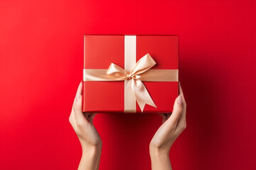 Top down view of a woman hands holding a luxury gift box with bow against a red background