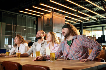 Excited sports fans, friends meeting at pub, drinking beer, watching football match on TV and shouting, cheering up team. Concept of sport competition, hobby, lifestyle, human emotions, fun