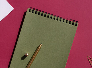 Green spiral notebook with white note paper, pen on the purple background. Copy space