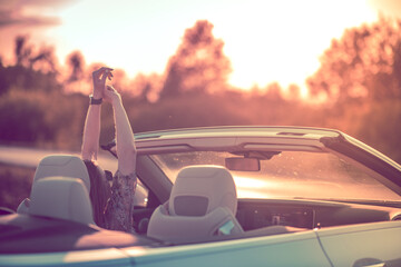 Freedom after a breakup. Young woman with the steering wheel of a convertible driving towards the setting sun.