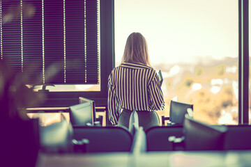 Pensive head of department looking into the distance through the window. Visible workstations.