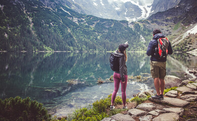 A couple of tourists during a trip to the mountains by a mountain lake. Girl pointing towards the mountain.