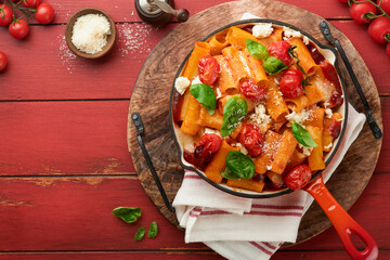 Pasta Tortiglioni with tomato sauce, baked cherry tomatoes, mozzarella and parmesan cheese, basil on old red rustic table. Traditional Italian cuisine. Example Italian food for article. Top view.
