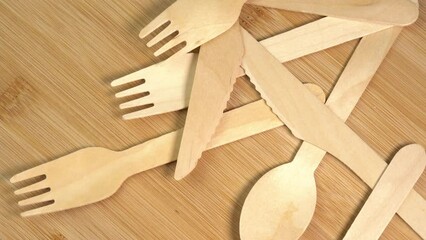 Wooden eco-friendly disposable tableware falling on the table. Pile of wooden spoons, forks and knives on cutting board surface. Disposable ecological tableware for kitchen and restaurant - Powered by Adobe