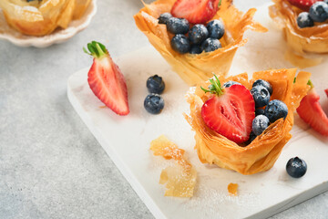 Phyllo or filo pies with fresh berries strawberries and blueberries, cheese filling topped with fresh mint on white plate. Homemade Filo pastry paskets. Delicious filo pastry dessert.
