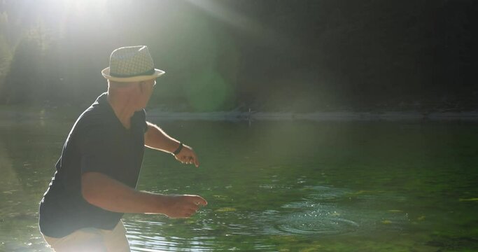 A man in the sun throws stones on the water on the lake. Rear view