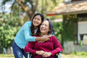 Naklejka premium Asian senior woman in wheelchair with happy daughter. Family relationship retired woman sitting on wheelchair in the park age care at retirement home.