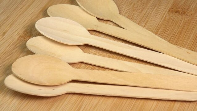 Row of wooden spoons on cutting board surface. Wooden eco-friendly disposable tableware rotate. Disposable ecological tableware for kitchen and restaurant