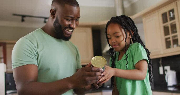 Happy african american father and daughter reading label on can in kitchen