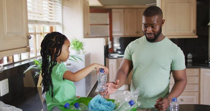 Happy african american father and daughter sorting recycling and crushing plastic bottles in kitchen