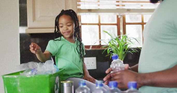 African american father and daughter sorting plastic bottles for recycling in kitchen