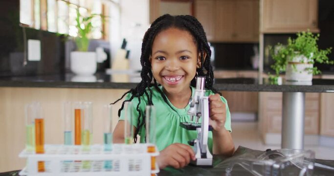Happy african american girl using microscope, doing experiments at home
