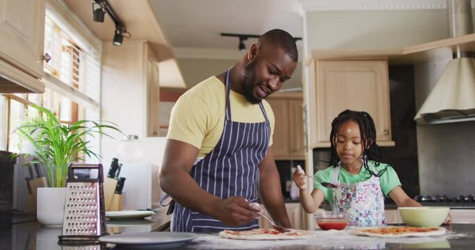Happy african american father and daughter preparing pizza in kitchen