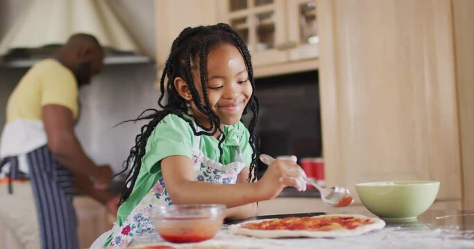 Happy african american daughter preparing pizza in kitchen with father