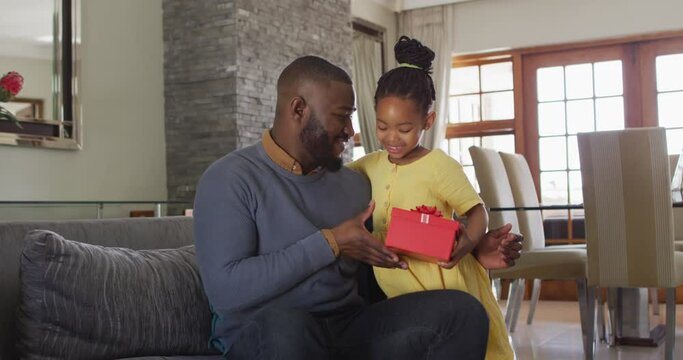 Happy african american daughter giving present to surprised father