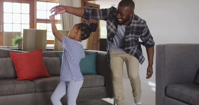 Happy african american daughter and father having fun, dancing in living room