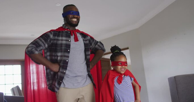 Happy african american father and daughter having fun, wearing superhero costumes