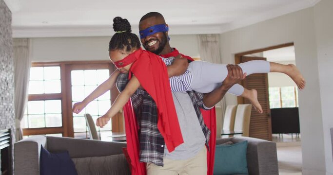 Happy african american father and daughter having fun, wearing superhero costumes