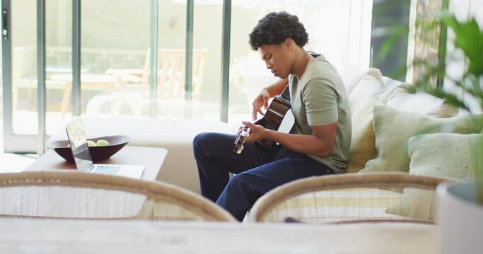 African american man plays guitar and singing, using laptop at home
