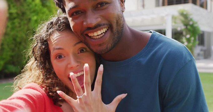 Happy biracial couple taking selfie in garden after proposal
