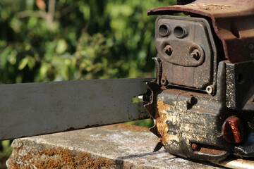 Old gasoline powered woodcutting machine with a view of its rusty engine exhaust. Rusty chainsaw machine on outdoors