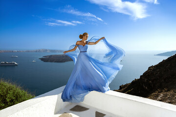 Glamour, stylish elegant woman in long gown dress is posing near Skaros Rock in luxury resort in...