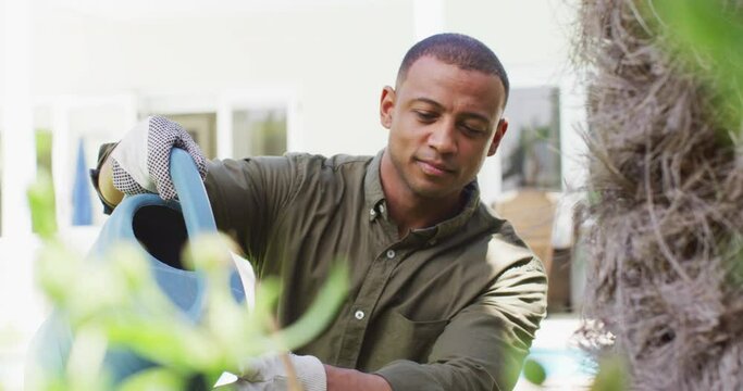Portrait of biracial man gardening, watering plants with watering can