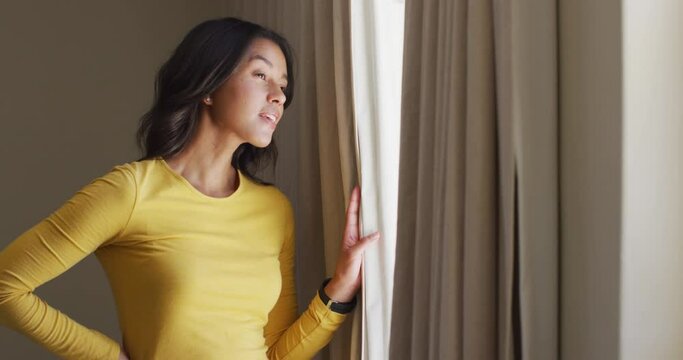Curious biracial woman revealing curtains and looking outside window