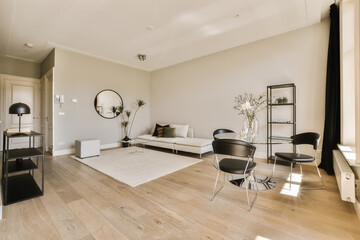 a living room with white walls and wood flooring in the center of the room, there is a large mirror on the wall