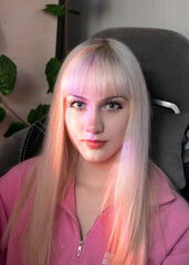 A blonde girl with long hair with straight bangs in a pink blouse smiles