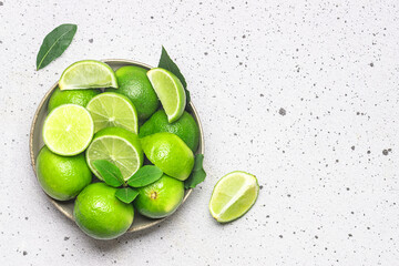 Ceramic bowl with limes on light stone background top view. Copy space for your design.
