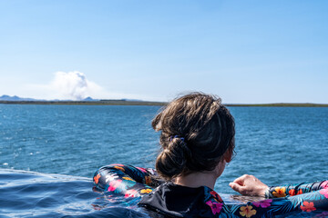 Woman at the hot spring sky lagoon relaxes in the infinity pool, overlooking the Atlantic Ocean, watching a volcano erupt in Iceland © MelissaMN