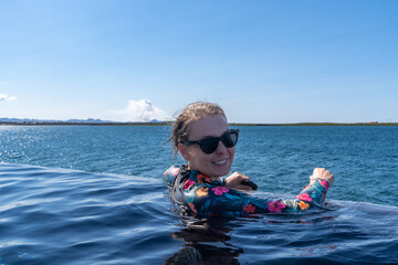 Woman in the hot spring in Iceland, infinity pool, as a volcano erupts in the background