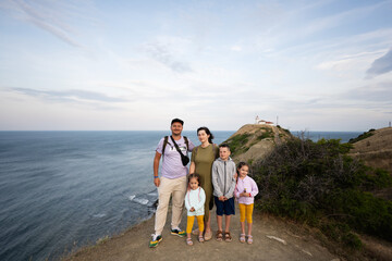 Happy family on the top of a mountain with a lighthouse in the background. Cape Emine, Black sea coast, Bulgaria.