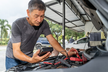Fototapeta na wymiar A middle age Asian male mechanic using a battery tester to check on car battery status